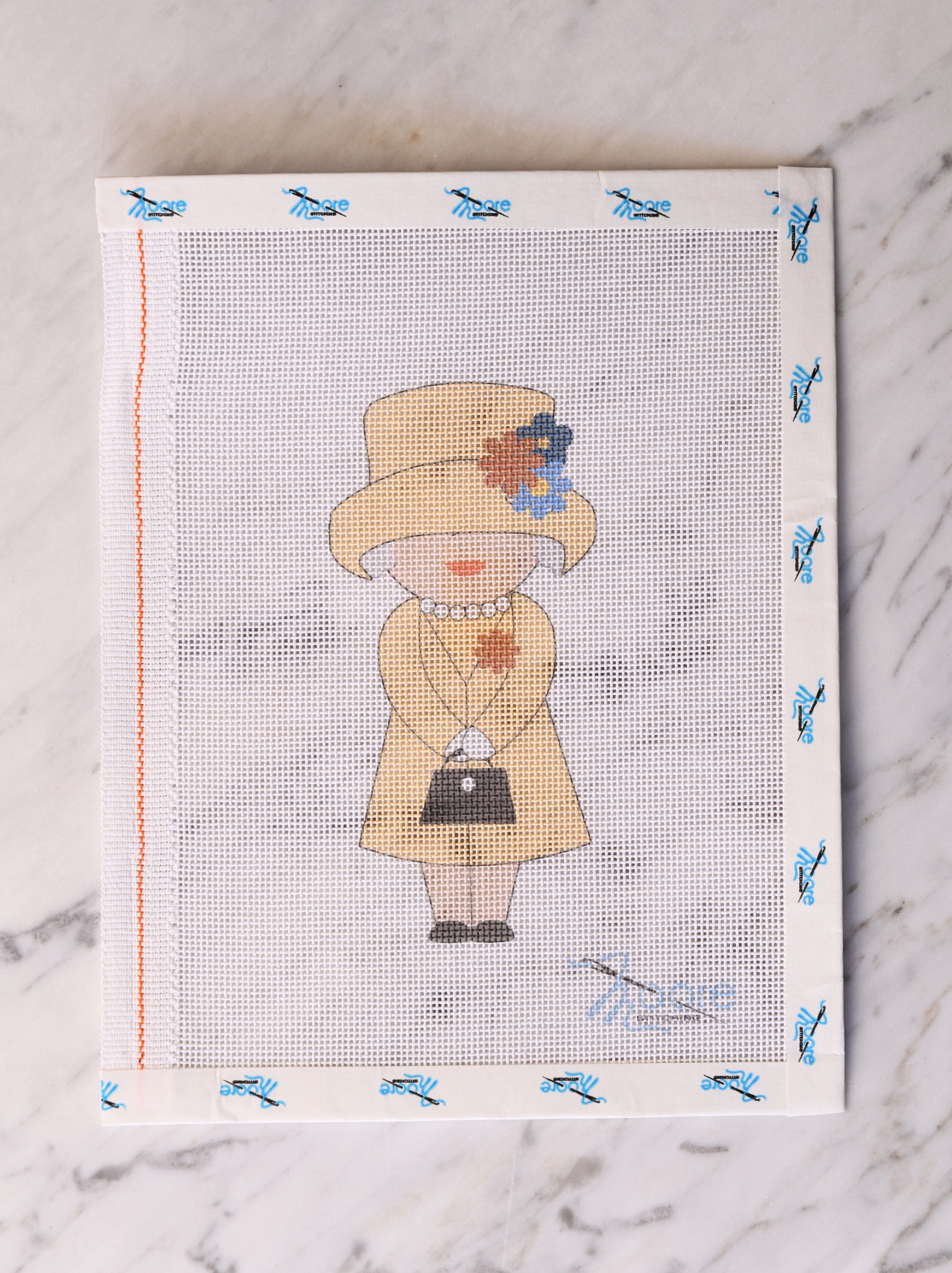 Cross-stitched design of a person wearing a hat and coat on fabric with decorative border.