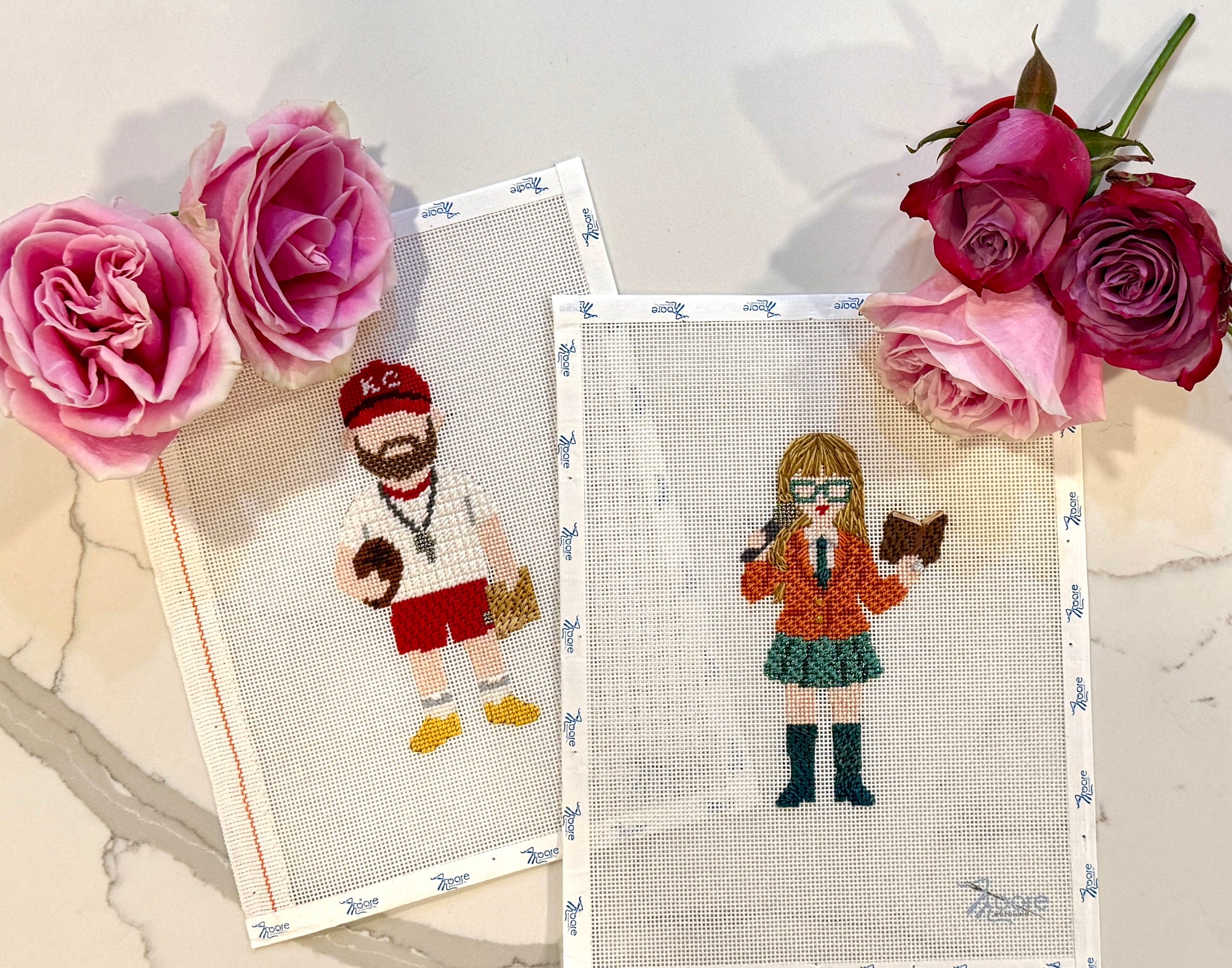 Two cross-stitched pieces of a man and a woman with flowers on a marble surface