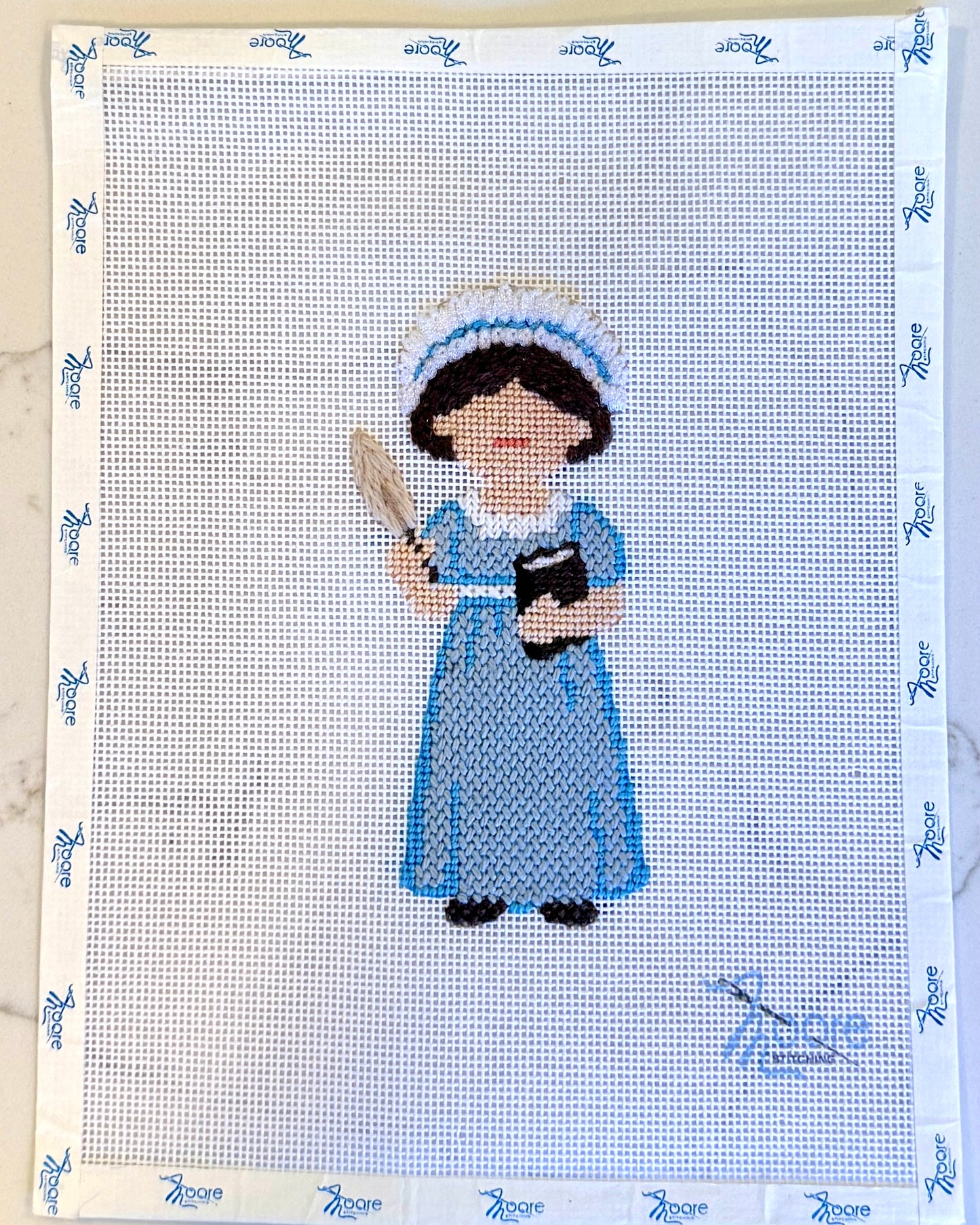 Cross-stitched design of Jane Austen in blue attire on fabric with a patterned border.