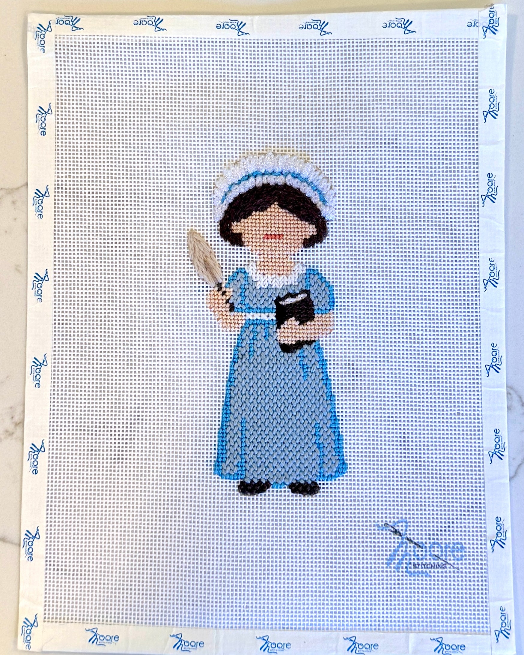 Cross-stitched design of Jane Austen in blue attire on fabric with a patterned border.