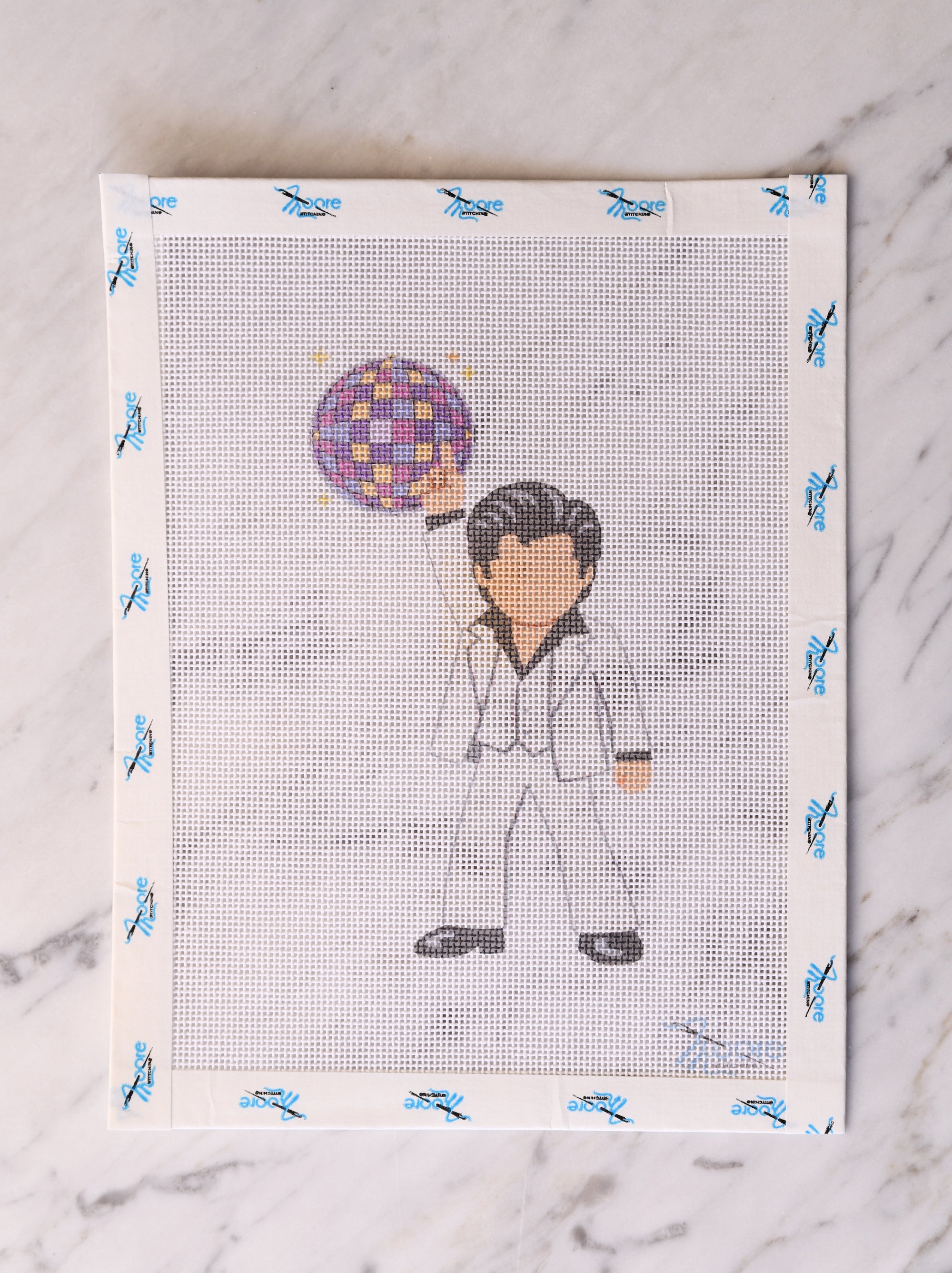 Cross-stitched design of a person with a colorful mirror ball on a white fabric background.