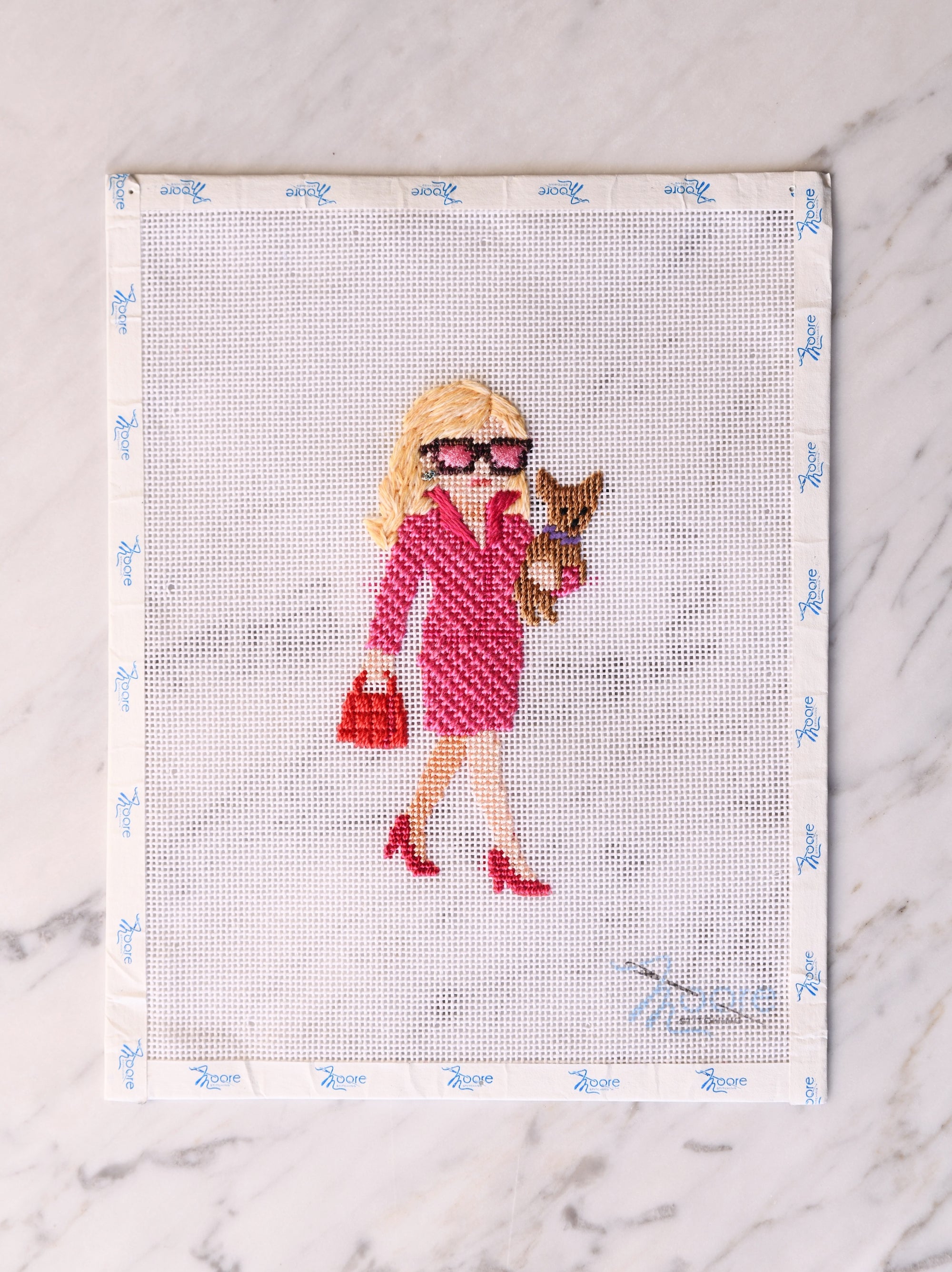 Cross-stitched picture of a woman in a pink and red dress with a dog on a white background