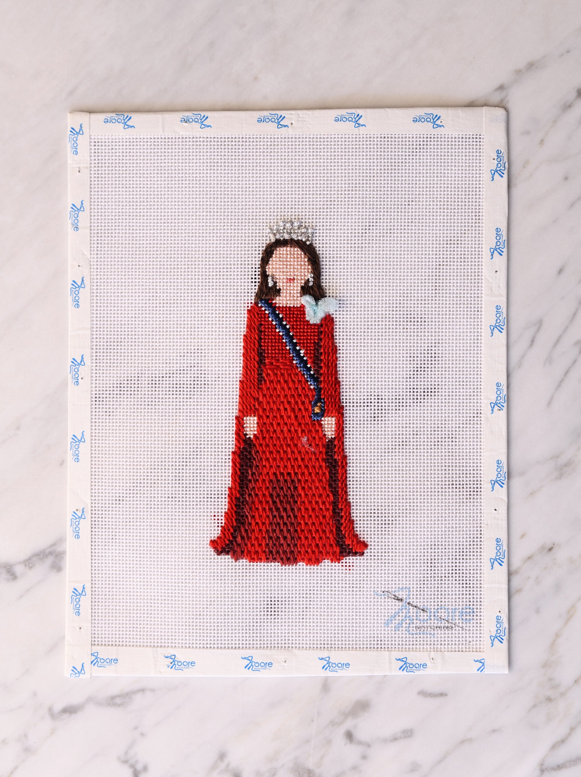 Cross-stitched portrait of a princess in a red dress on a white fabric background