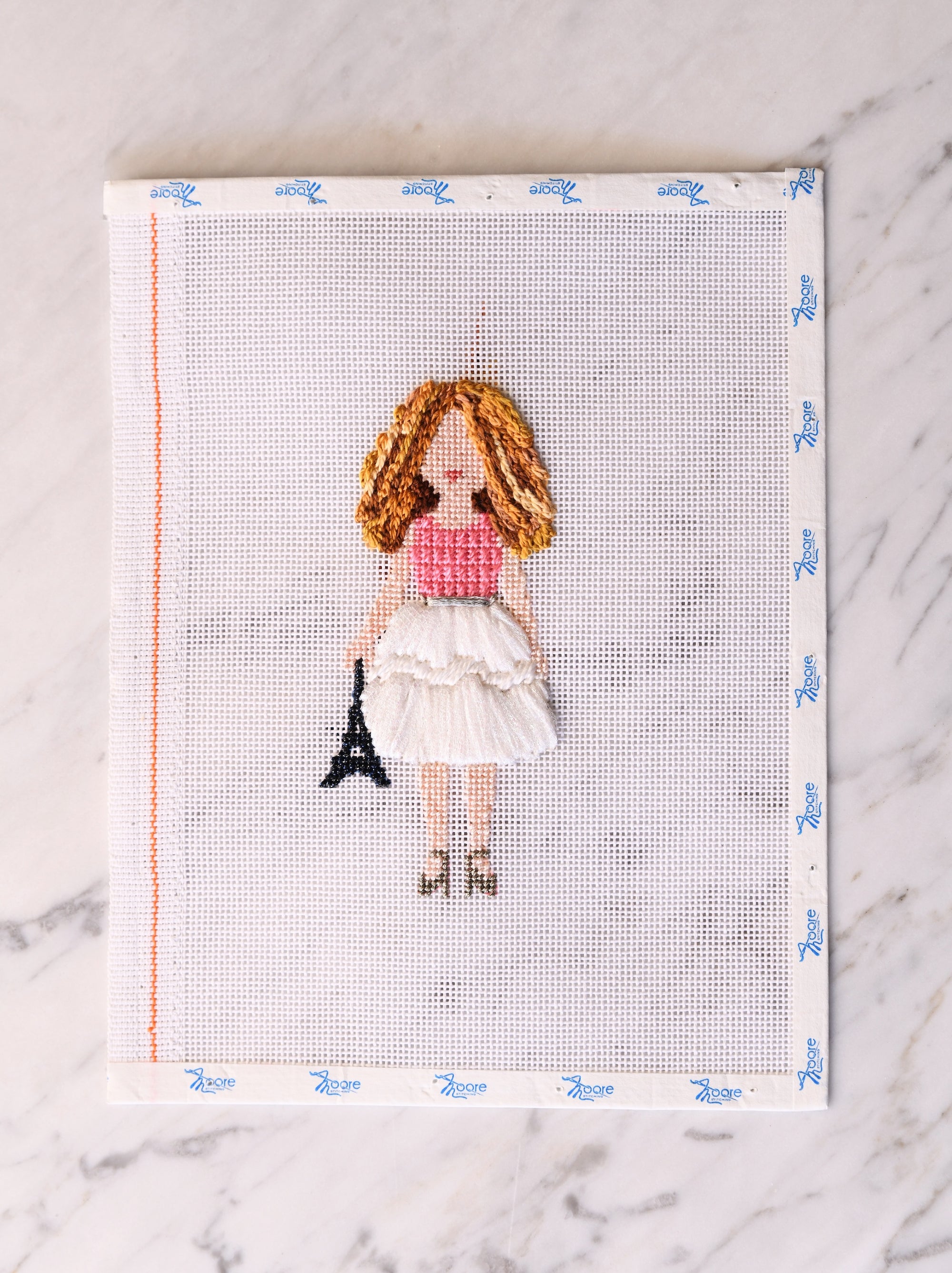 Cross-stitched design of a girl with the Eiffel Tower on fabric