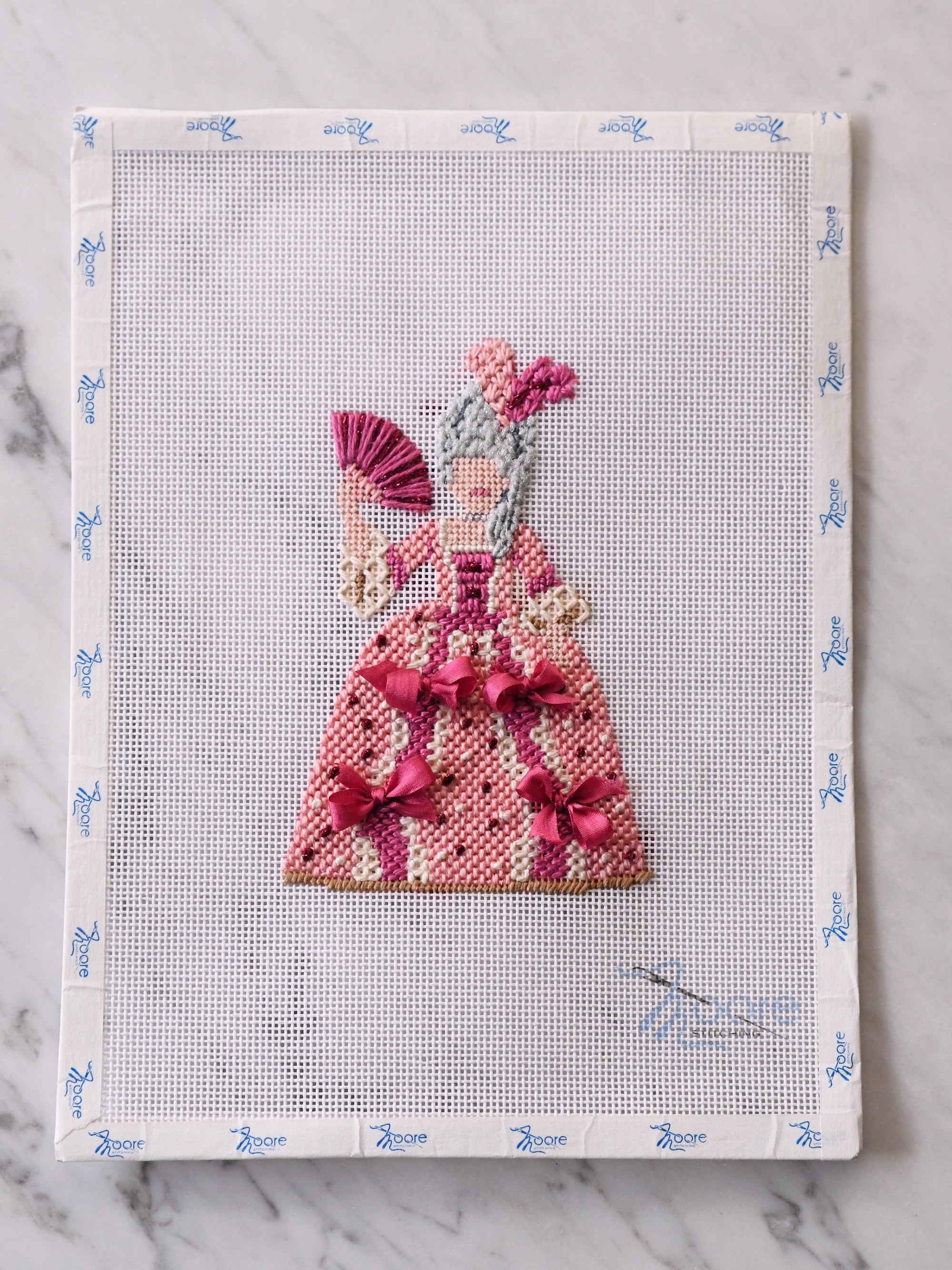 Cross-stitched dress design on a fabric swatch with a grid pattern.