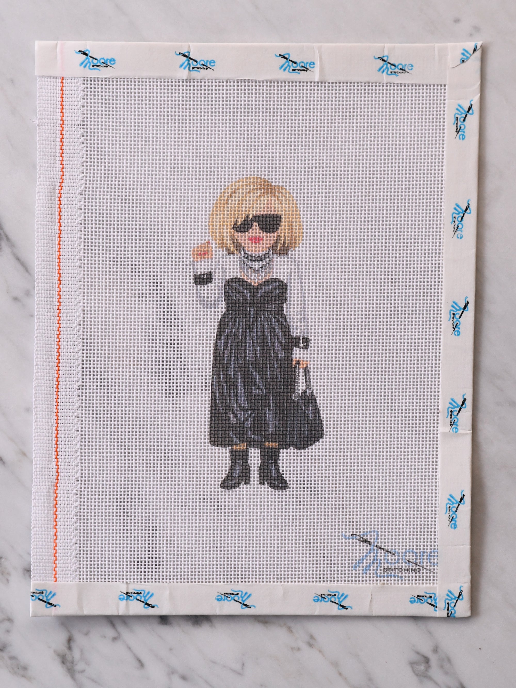 Cross-stitched artwork of a woman in a black dress on mesh fabric.