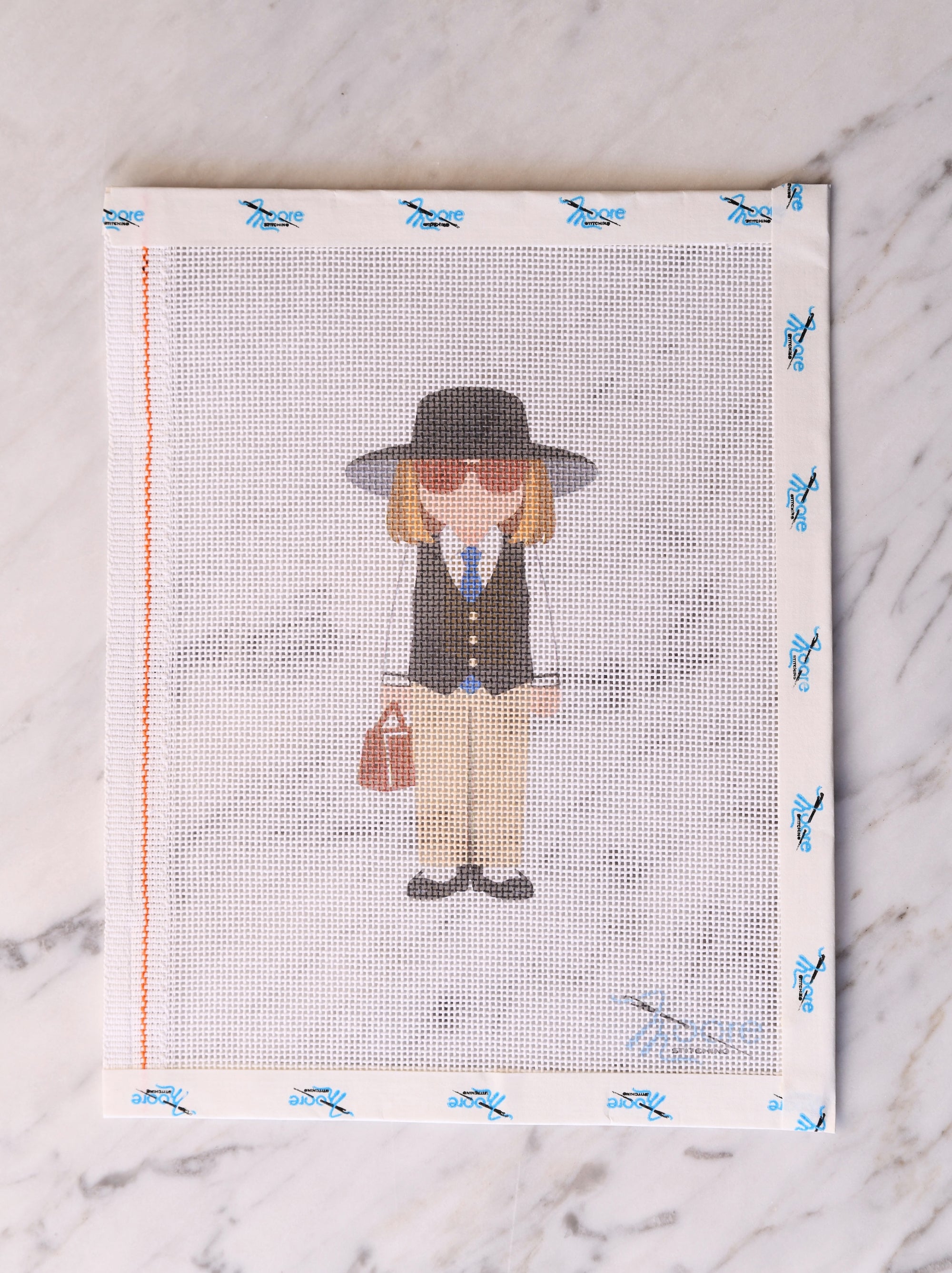 Cross-stitched pattern of a person with a hat and briefcase on fabric with butterfly designs.
