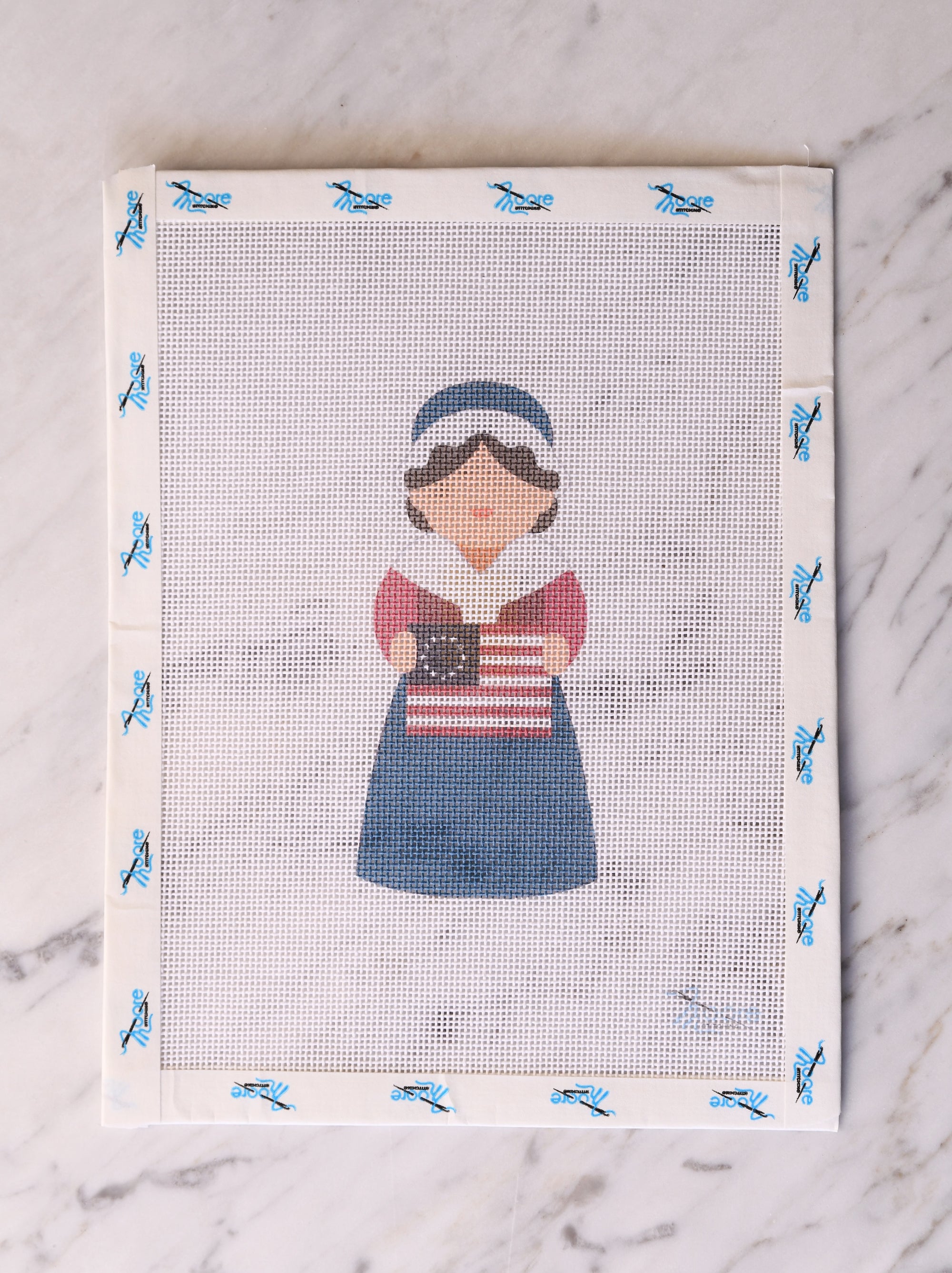 Cross-stitched design of a person holding an American flag on a white fabric background.