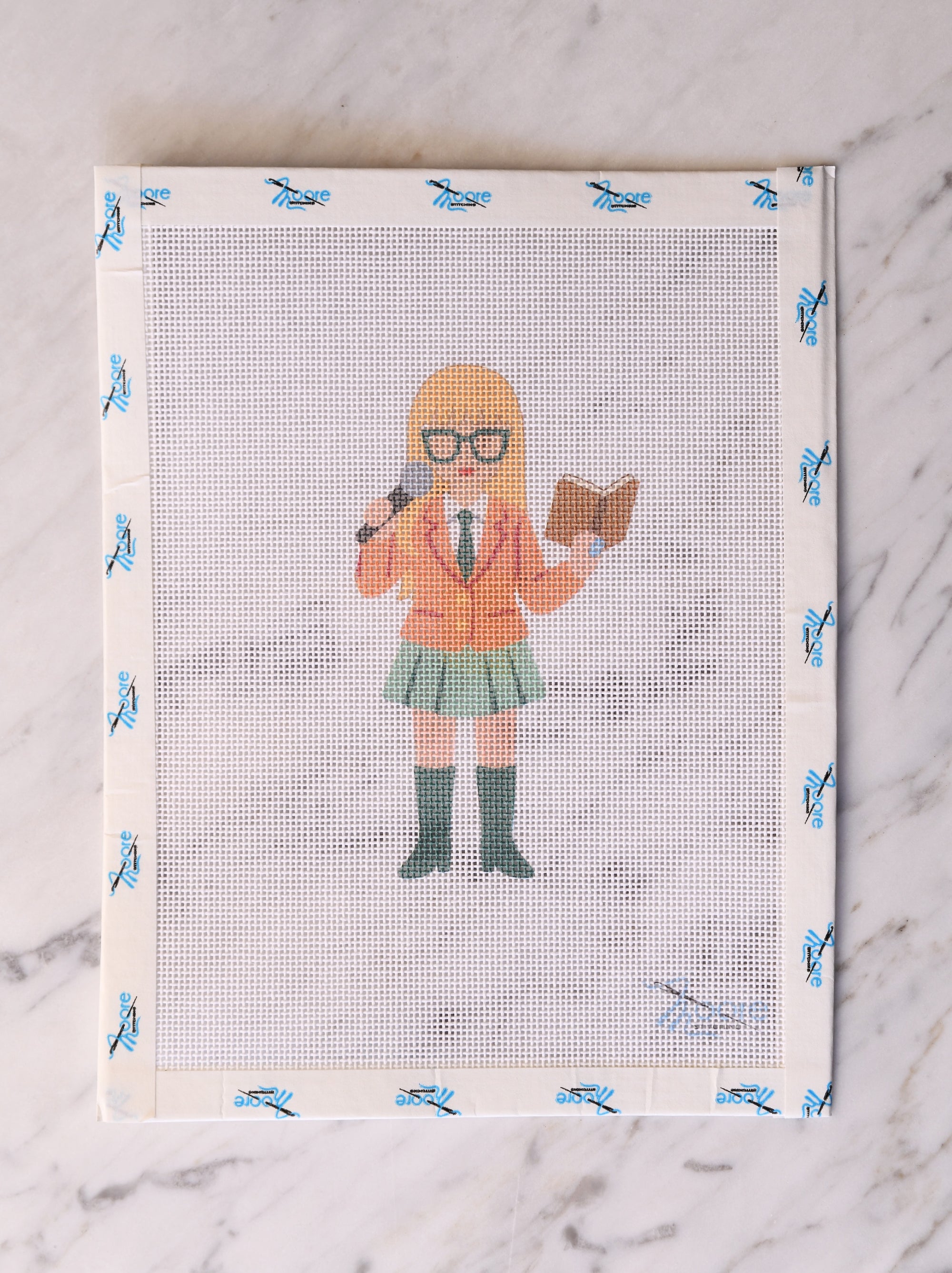 Cross-stitched design of a person with a microphone and book on a textured surface