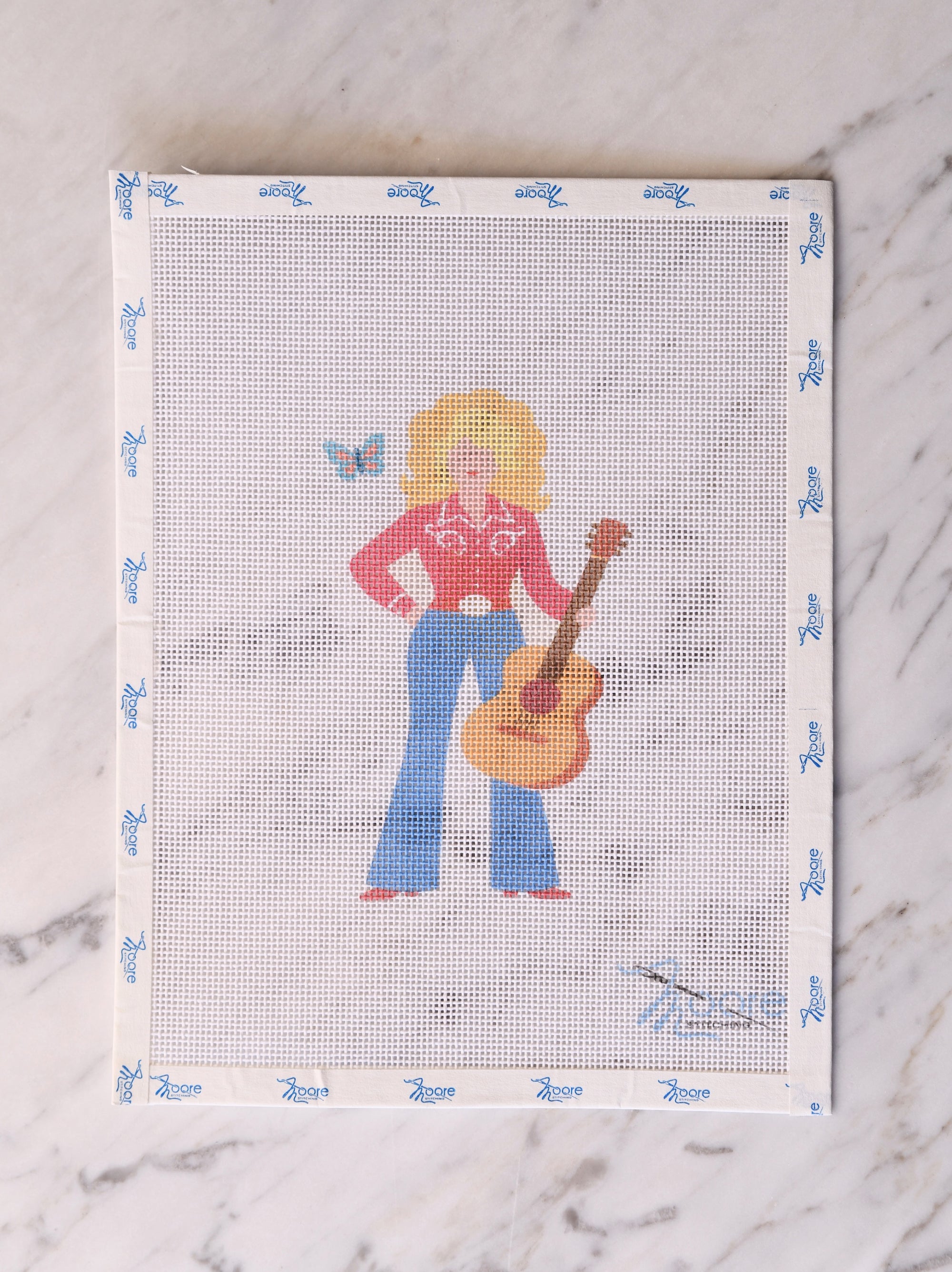 Cross-stitched pattern of a country girl with a guitar on fabric.