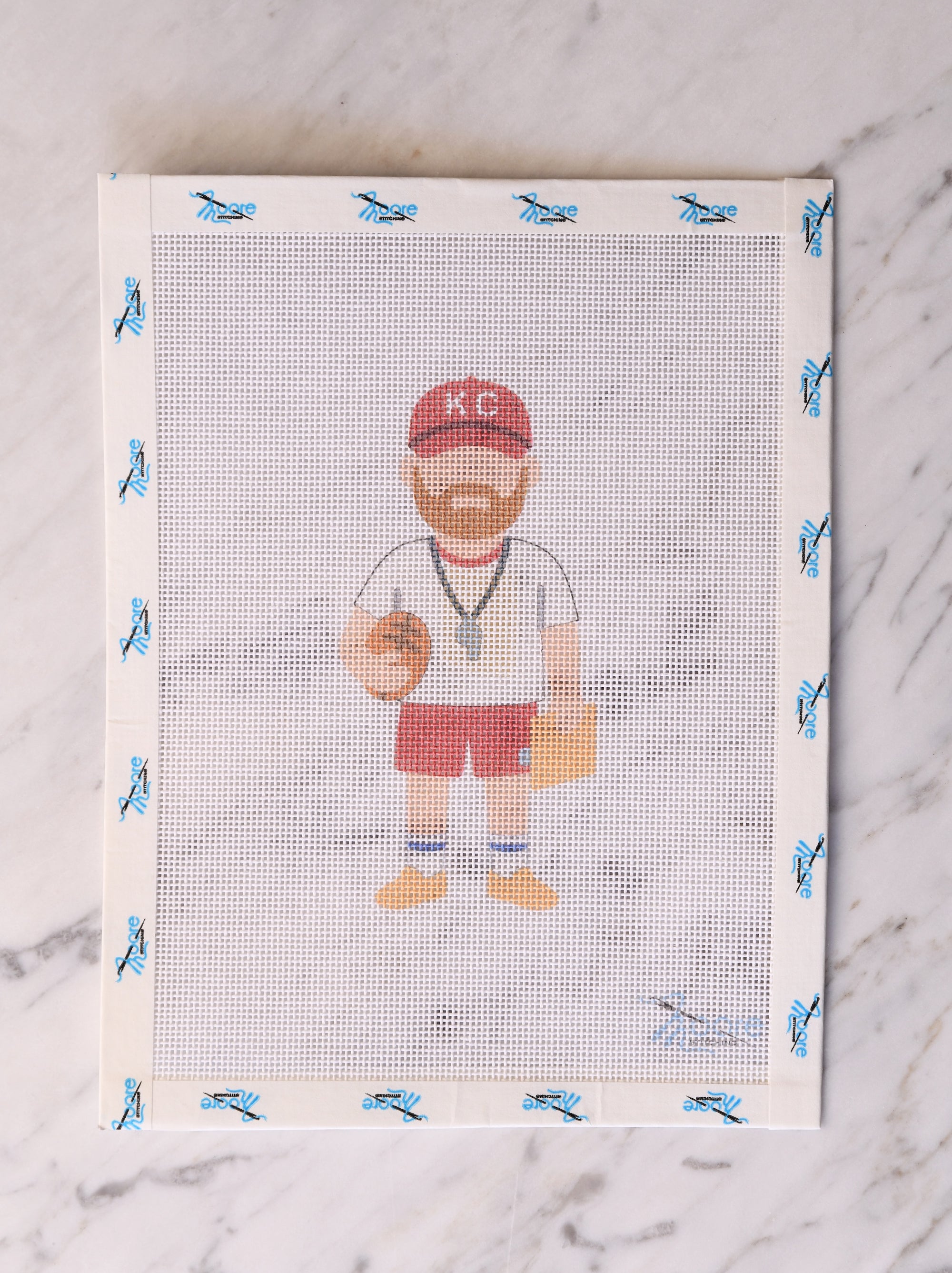 Cross-stitched design of a coach holding a football on a mesh fabric.