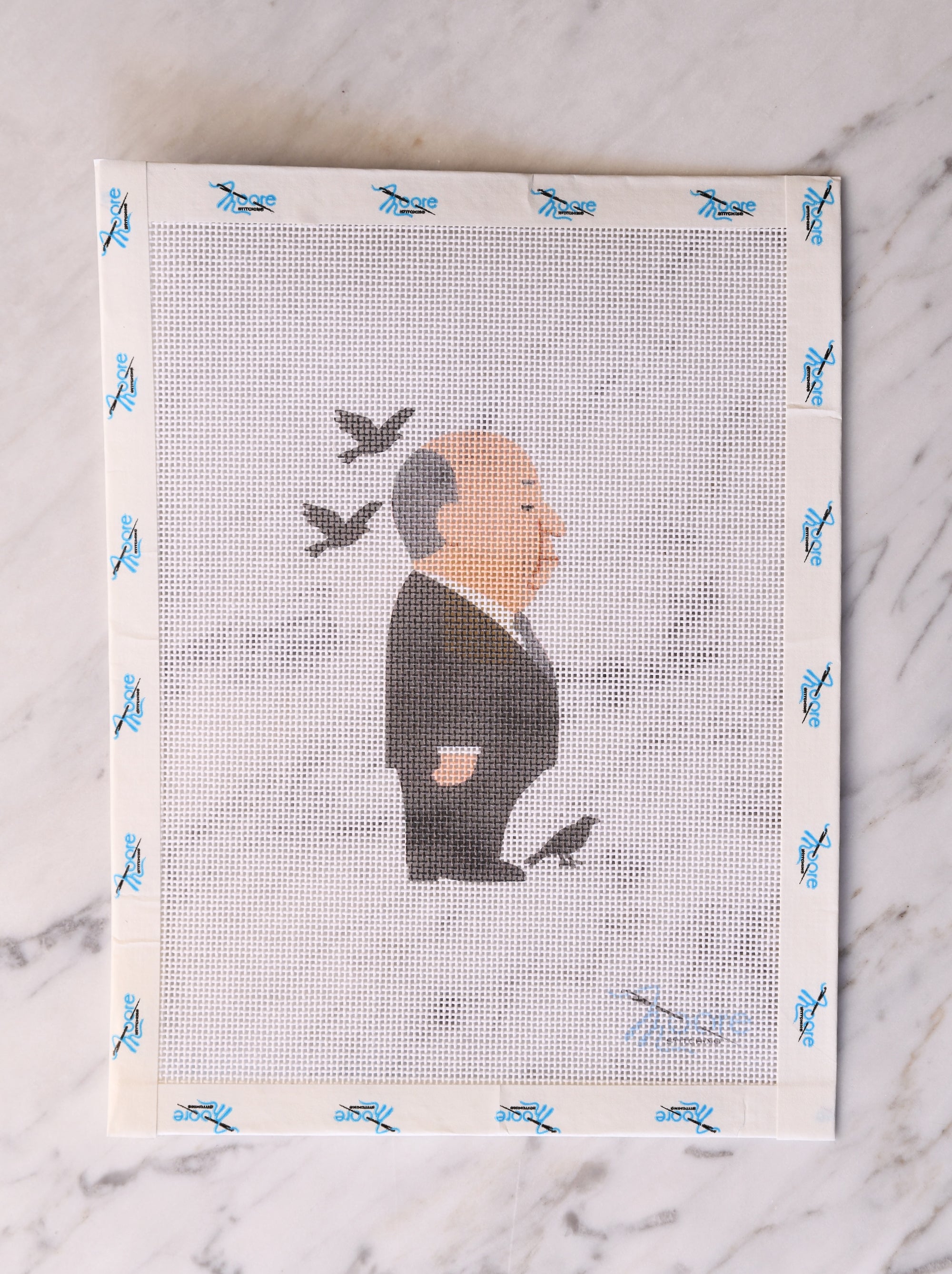 Cross-stitched portrait of a man with birds on a framed piece of fabric.