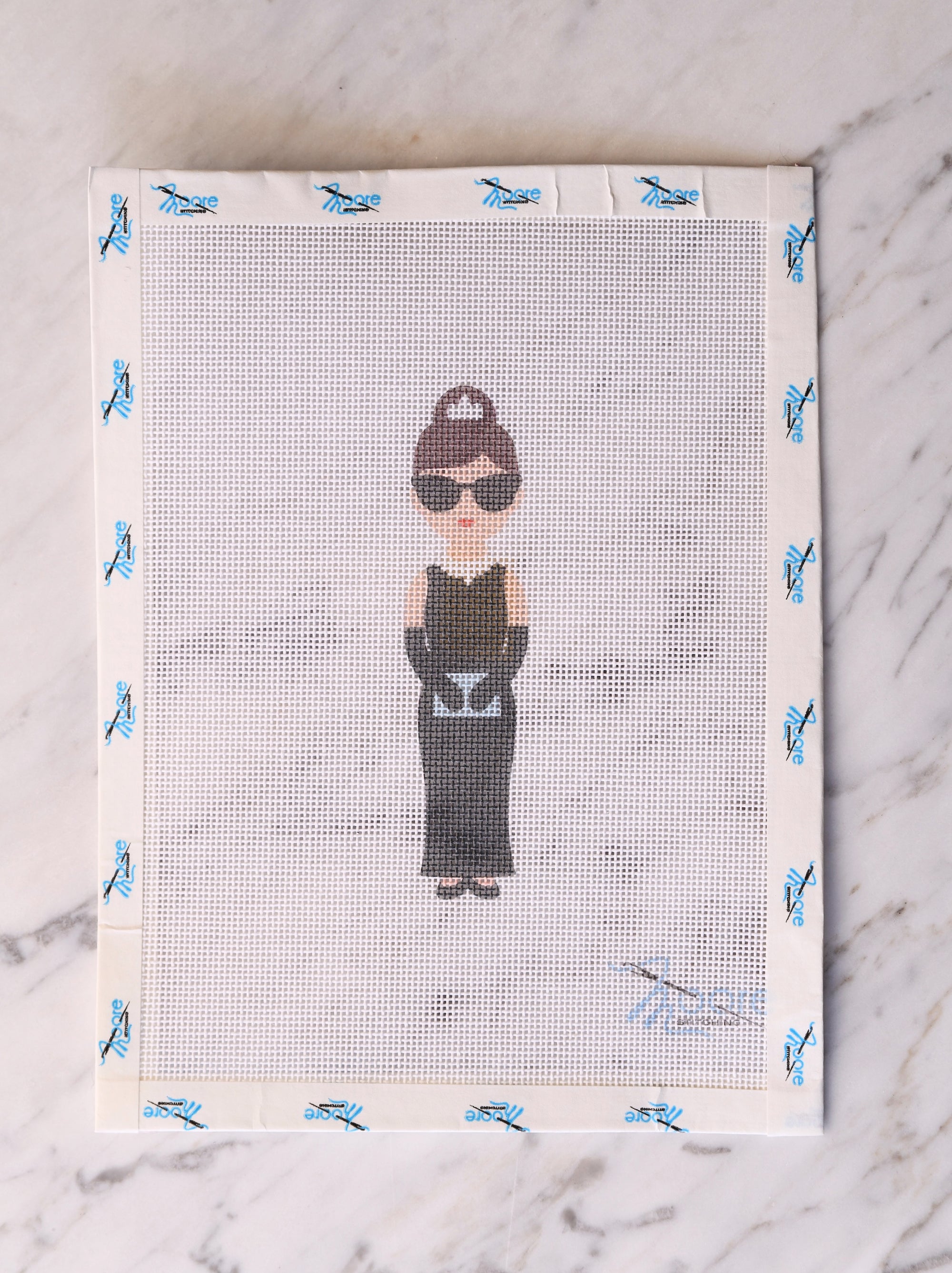 Cross-stitched design of a woman in a black dress and hat on fabric.