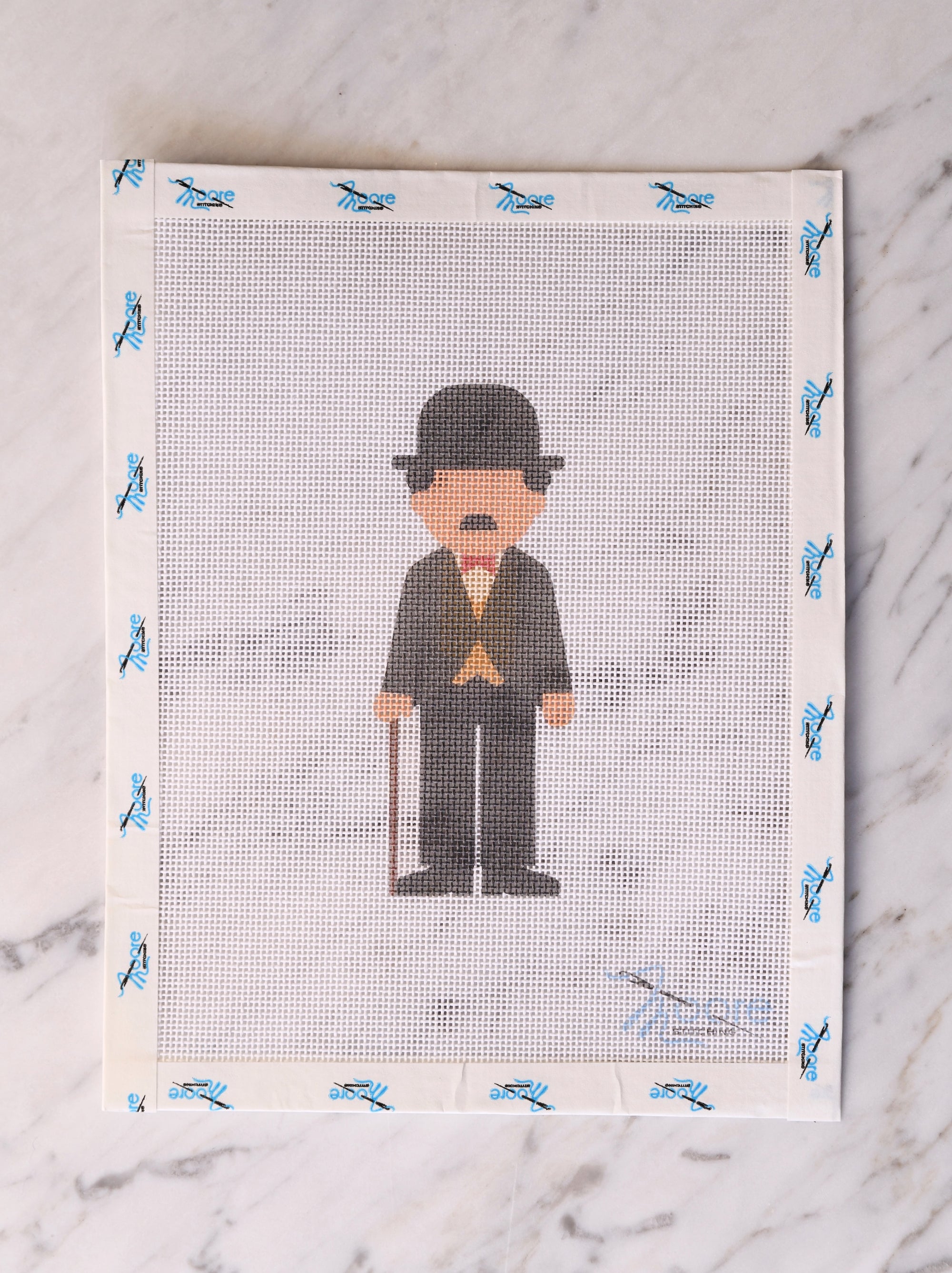 Cross-stitched pattern of a man with a hat and cane on fabric.