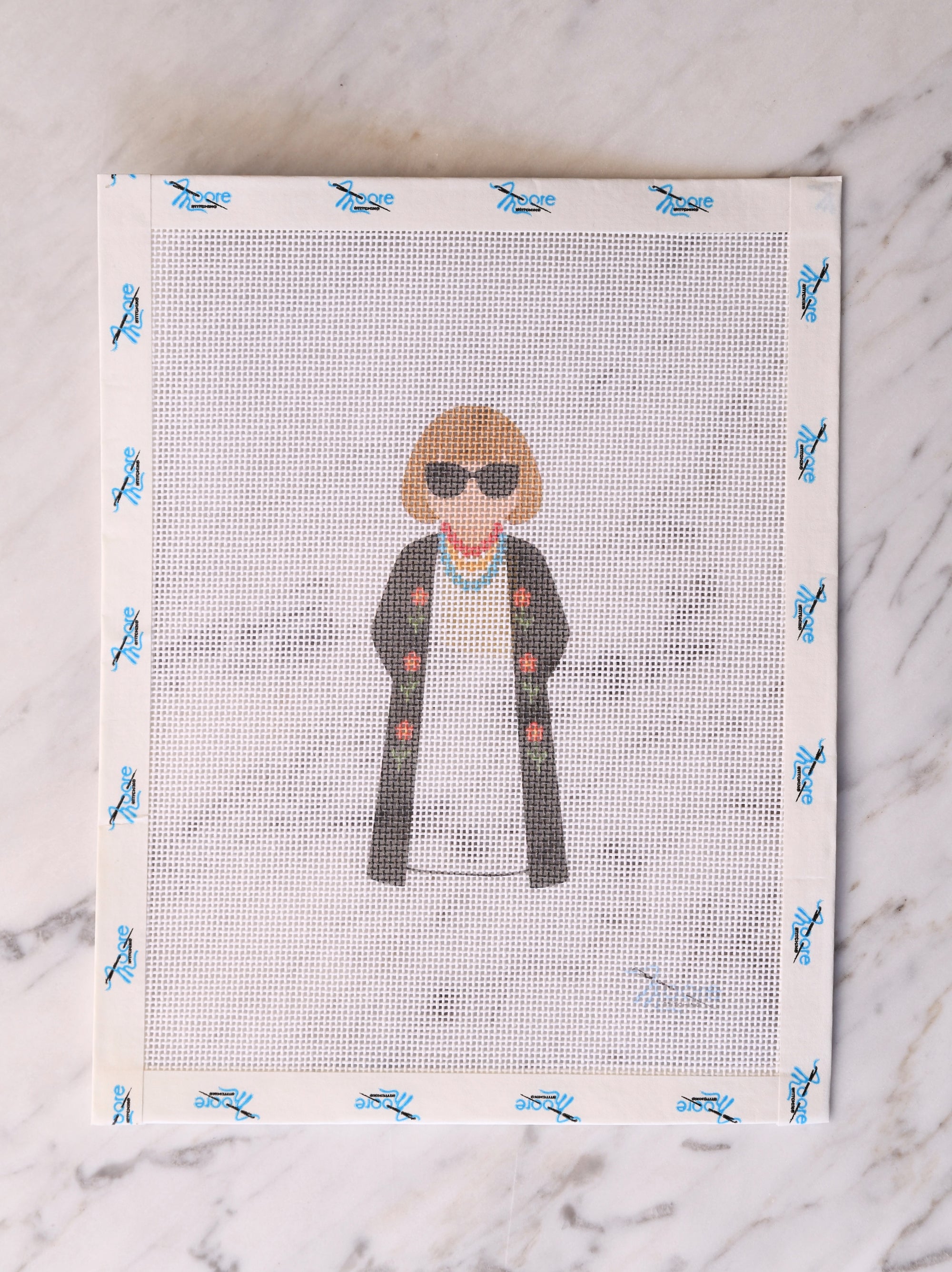 Cross-stitched pattern of a person wearing sunglasses and a jacket on a fabric swatch.