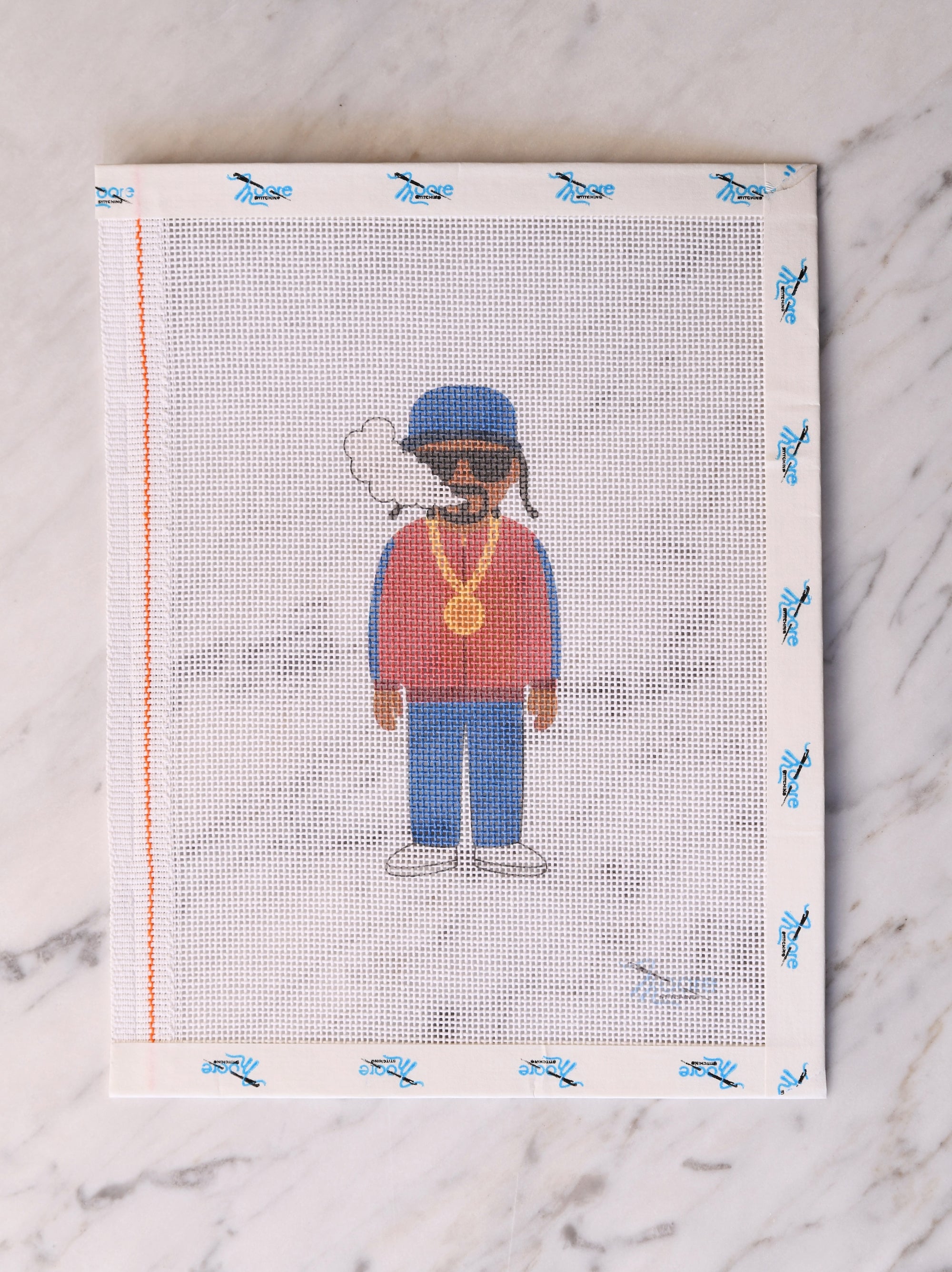 Cross-stitched pattern of a person wearing a red shirt, blue pants, and a blue cap on a white fabric background.