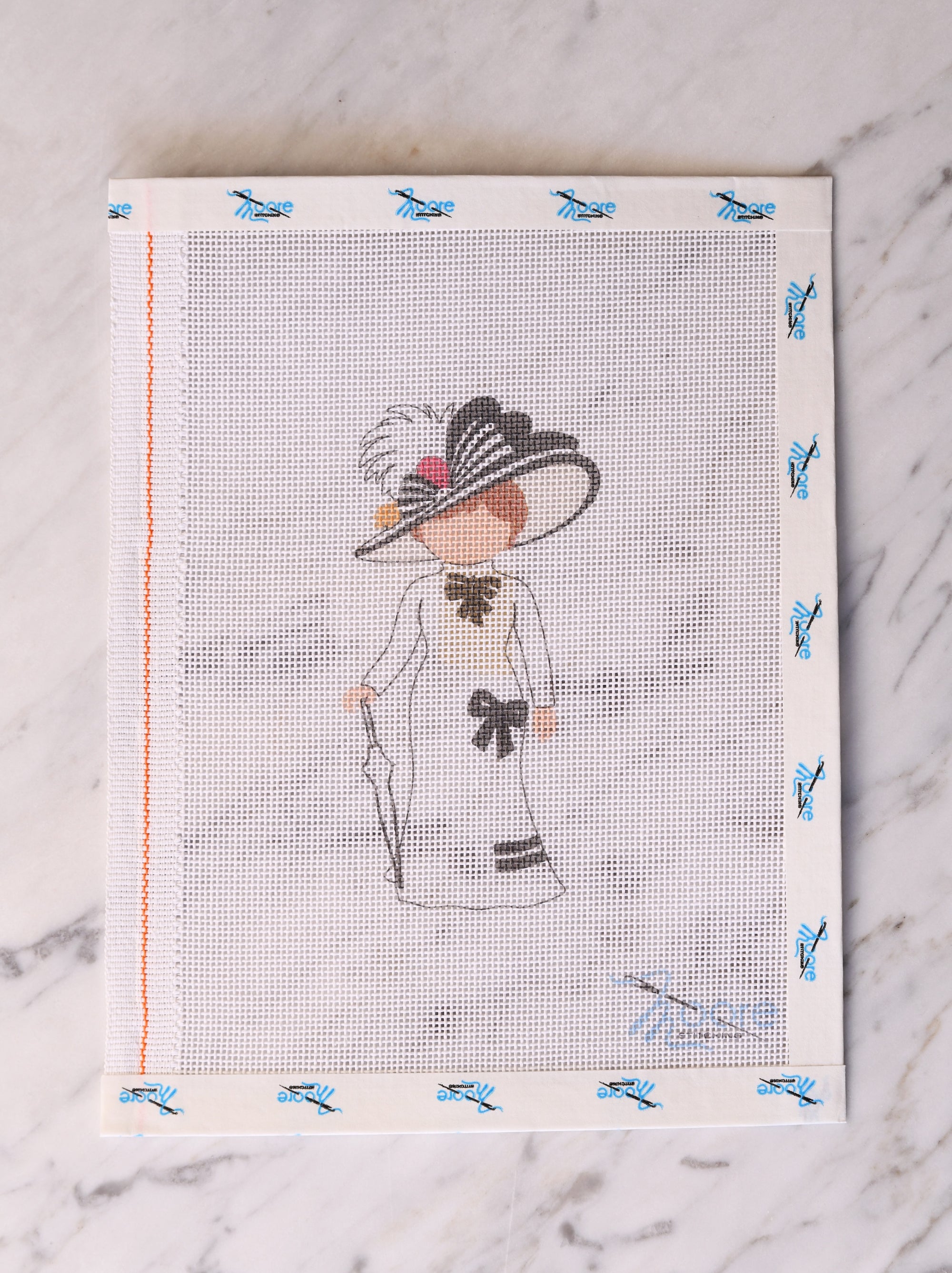 Cross-stitched design of a woman in a hat and dress on fabric.