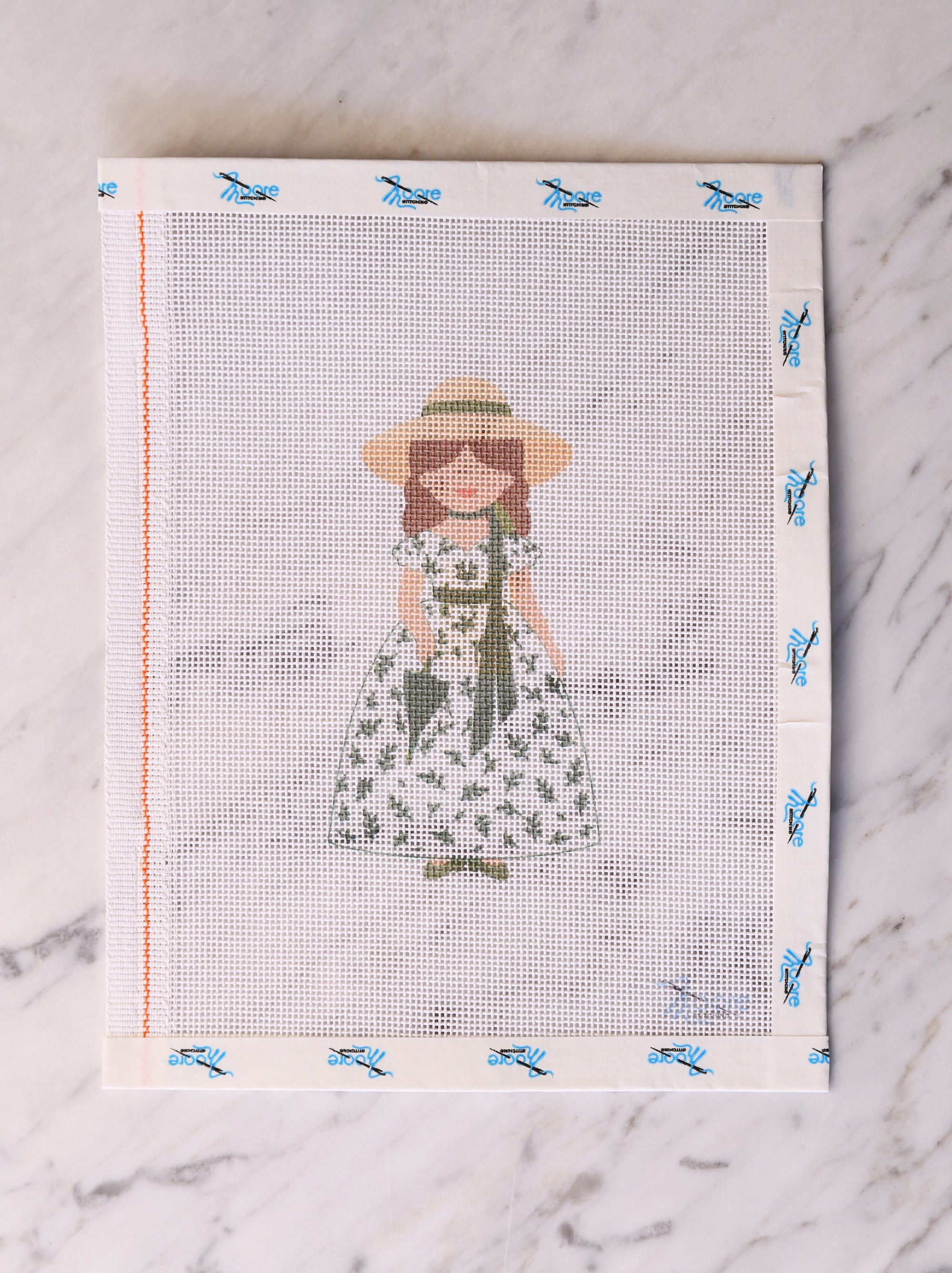 Cross-stitch pattern with a woman in a dress and hat on a white fabric background.