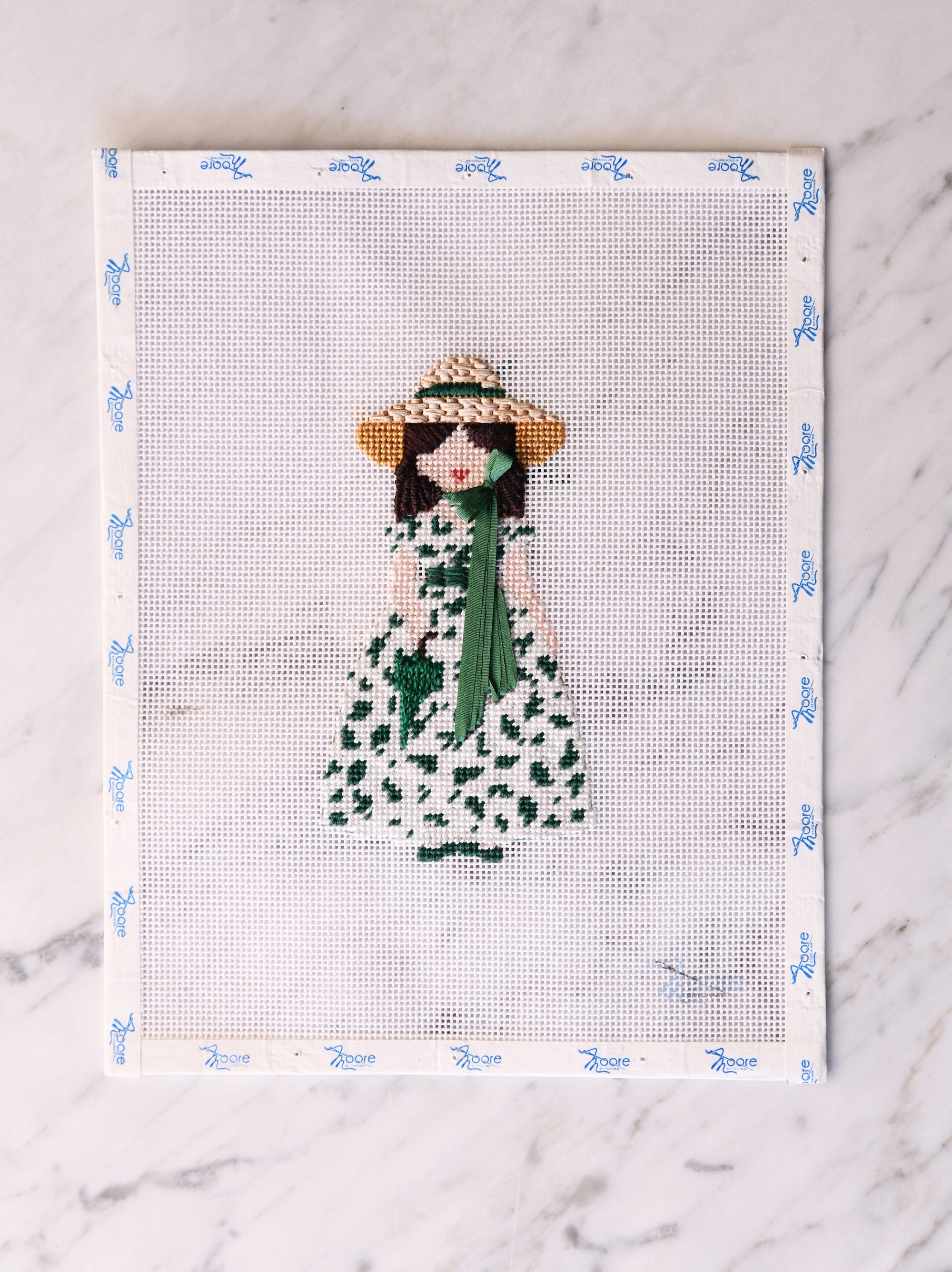 Cross-stitched design of a woman in a dress and hat on fabric with a white background