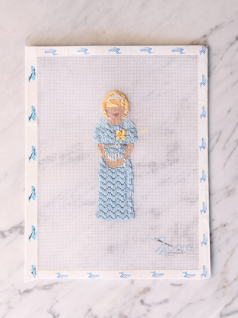 Cross-stitched design of a woman holding a baby on fabric with a white border.