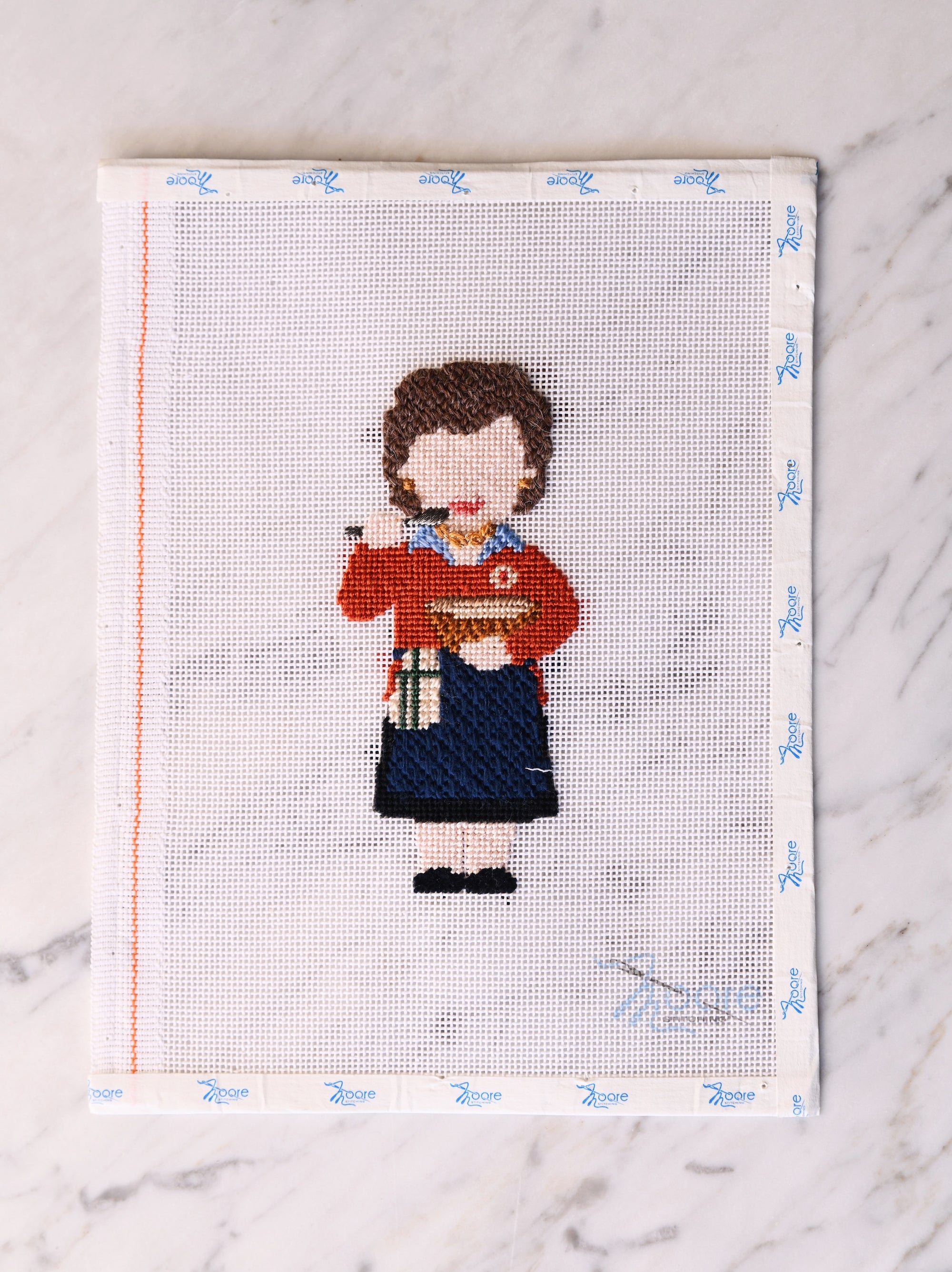 Cross-stitched design of a woman holding a bowl and spoon on a white fabric background