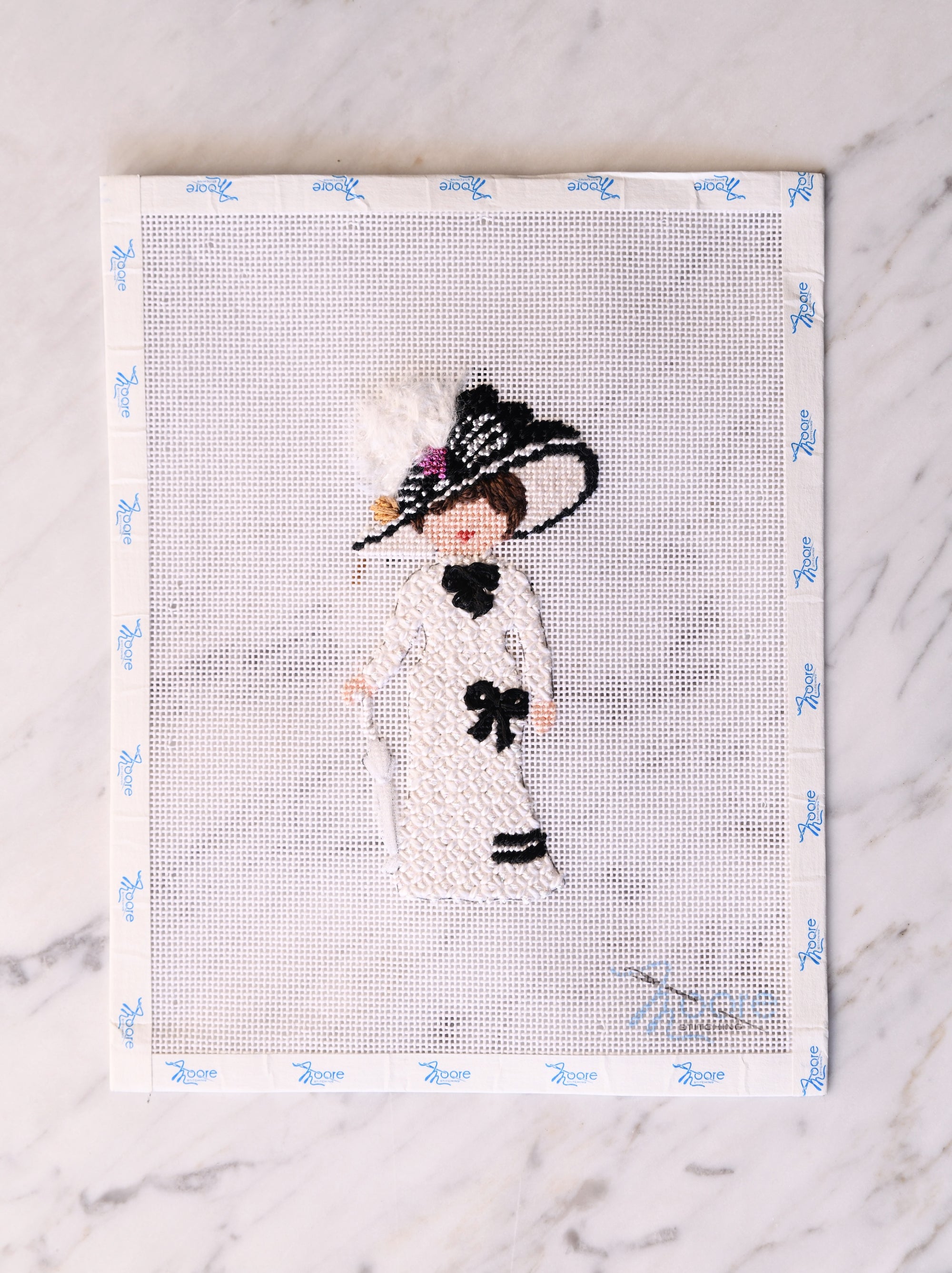 Cross-stitched portrait of a woman with a black hat on a white background
