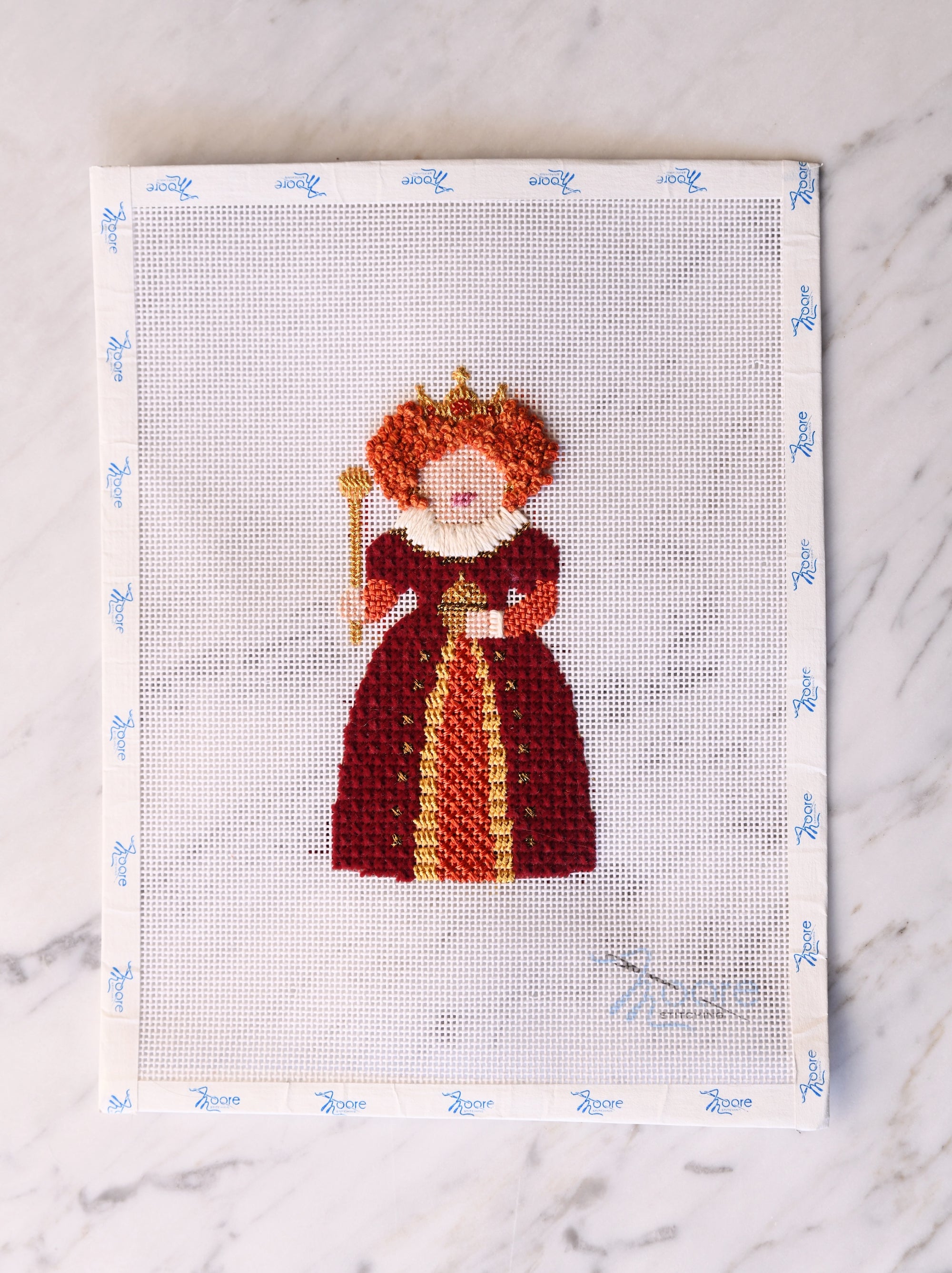 Cross-stitched design of a queen in a red dress and crown on a white background.