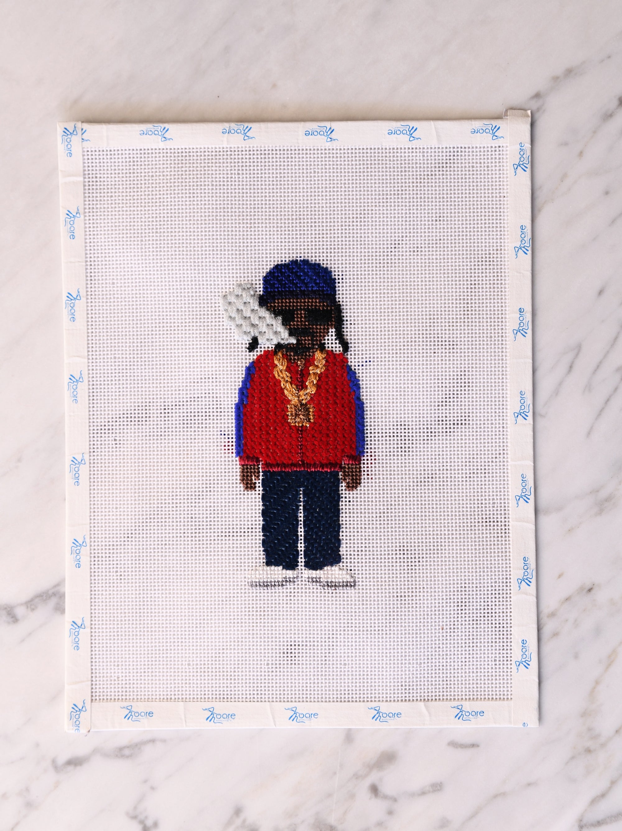 Cross-stitched figure of a person wearing a red sweater and blue hat on a white background